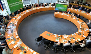 Ein großer, runder Konferenztisch mit vielen Teilnehmer:innen im Bundestag. Im Hintergrund sind große Fenster mit Blick auf das Paul-Löbe-Haus zu sehen.