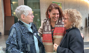 Drei Frauen stehen an einem Tisch. Beate Müller-Gemmeke diskutiert mit einer Frau, während eine weitere Frau zuhört.