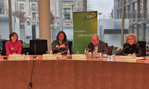 Beate Müller-Gemmeke spricht bei einer Podiumsdiskussion mit weiteren Teilnehmer:innen. Im Hintergrund der Bundestag und ein Roll-Up mit dem Schriftzug „Uns geht's ums Ganze“.