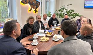 Beate Müller-Gemmeke und mehrere Männer sitzen an einem Konferenztisch mit Tassen und Gebäck. An der Wand hängt eine beleuchtete Landkarte der Ukraine.