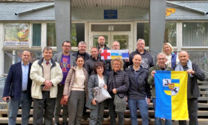 Eine Gruppe von Männern und Frauen posiert vor der Universität. Einige halten die ukrainische Flagge und ein Schild mit dem Logo von „Ermstal hilft“. Alle lächeln in die Kamera.