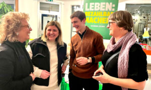 Beate Müller-Gemmeke unterhält sich mit drei Menschen. Alle lachen und wirken in einer lebhaften, freundlichen Stimmung. Im Hintergrund sind grüne Wahlkampfplakate zu sehen.