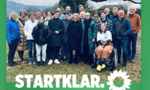 Gruppenfoto von Beate Müller-Gemmeke mit Jaron Immer und weiteren Unterstützer:innen der Grünen. Alle stehen lächelnd vor einem Baum im Freien. Im Vordergrund ist der Schriftzug "STARTKLAR." mit dem Grünen-Logo zu sehen. Die Stimmung wirkt entschlossen und motiviert.