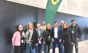 Gruppenfoto von mehreren Mitgliedern von GewerkschaftsGrün unter einer Parteifahne mit Sonnenblumen-Logo. Beate Müller-Gemmeke steht in der Mitte neben Felix Banaszak, flankiert von weiteren Delegierten, die entspannt und freundlich in die Kamera blicken.