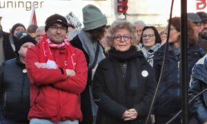 Beate Müller-Gemmeke steht auf einer Demonstration neben einem Mann in roter Jacke und Schal. Beide blicken konzentriert nach vorne. Im Hintergrund sind weitere Demonstrierende zu sehen, einige halten Plakate.