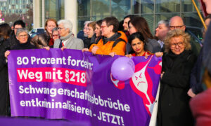 Eine Gruppe von Frauen steht vor dem Paul-Löbe-Haus in Berlin und hält ein lila Banner mit der Aufschrift: „80 Prozent fordern: Weg mit § 218 – Schwangerschaftsabbrüche entkriminalisieren – JETZT!“. Das Banner zeigt eine wütend blickende stilisierte Gebärmutter. Vor den Frauen stehen mehrere Kartons mit der Aufschrift „#wegmit218! Aktion jetzt“. Beate Müller-Gemmeke ist unter den Frauen. Im Hintergrund sind weitere Demonstrierende zu sehen.