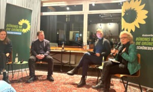 Vier Personen sitzen auf einer Podiumsdiskussion in einem Raum mit großen Fenstern. Beate Müller-Gemmeke, in einer grünen Jacke, spricht mit einem Mikrofon in der Hand. Neben ihr sitzt Moritz Heuberger, ganz in Schwarz, mit einem Tablet auf dem Schoß. Links sitzen zwei weitere Diskussionsteilnehmende, darunter Jan Otto von der IG Metall Berlin und Julia Jirmann vom Netzwerk Steuergerechtigkeit. Im Hintergrund stehen zwei grüne Banner von Bündnis 90/Die Grünen mit dem Logo der Partei.