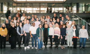 Eine große Gruppe von Menschen steht auf einer Treppe im Bundestag und blickt in die Kamera. Beate Müller-Gemmeke steht in der vorderen Reihe, umgeben von Besucher:innen ihrer BPA-Fahrt. Die Teilnehmenden wirken gut gelaunt und engagiert.