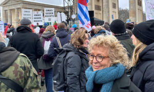 Beate Müller-Gemmeke steht mit einem blauen Schal lächelnd inmitten einer Demonstration vor dem Brandenburger Tor. Im Hintergrund sind Demonstrierende mit Schildern und Fahnen zu sehen, darunter „Omas gegen Rechts“.