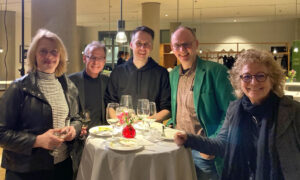 Beate Müller-Gemmeke steht mit vier weiteren Personen an einem runden Stehtisch mit Weingläsern und Tellern. Die Gruppe unterhält sich in entspannter Atmosphäre in einem elegant beleuchteten Raum. Alle wirken gut gelaunt.