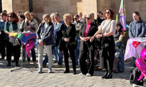 Beate Müller-Gemmeke steht mit anderen Frauen auf einem Platz vor einem historischen Gebäude mit gotischer Architektur. Einige tragen Sonnenbrillen, andere haben Fahnen oder bunte Accessoires. In der Mitte steht ein Pult mit einer Regenbogenfahne. Die Atmosphäre ist aufmerksam und konzentriert.